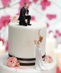 Bride waving to her groom while he sits on top of their cake
