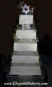 Square and elegantly tiered wedding cake is separated with pillars and has a large silver snowflake topper