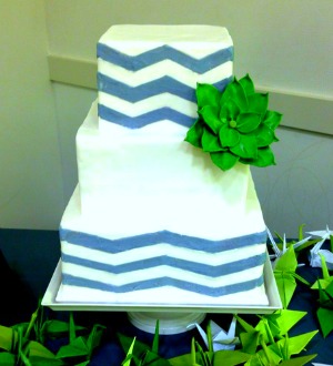 Three tier square white wedding cake with blue horizantal lines and green flower
